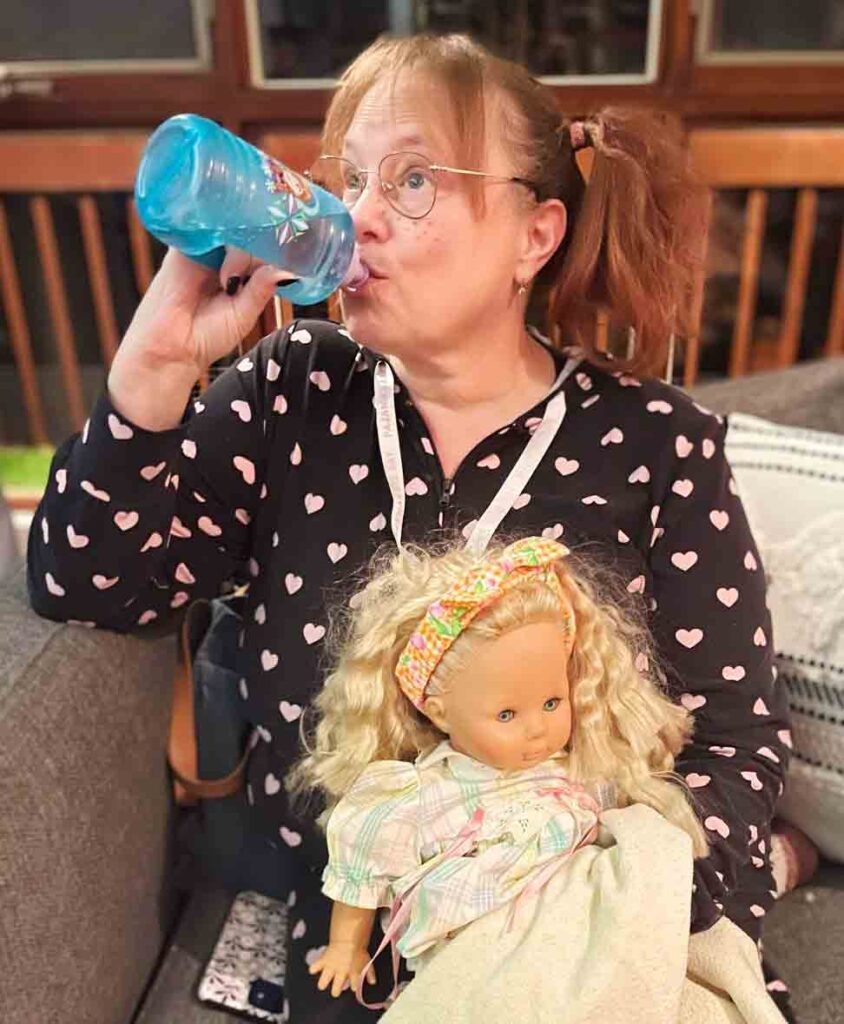Me in a long one-piece pyjama with my hair in pigtails, holding onto a doll and drinking from a sippy cup.